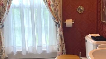 Un baño con inodoro, bidé y ventana con cortinas florales.