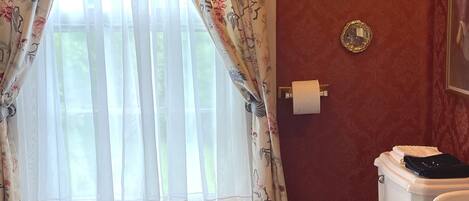 Un baño con inodoro, bidé y ventana con cortinas florales.