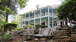 A two-story house with a porch, stone wall, and American flag. - The Sautee Inn Bed & Breakfast (Sautee Nacoochee)