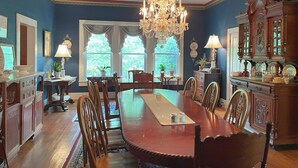 A dining room with a large wooden table, chairs, a chandelier, and a cabinet with dishes. - The Sautee Inn Bed & Breakfast (Sautee Nacoochee)