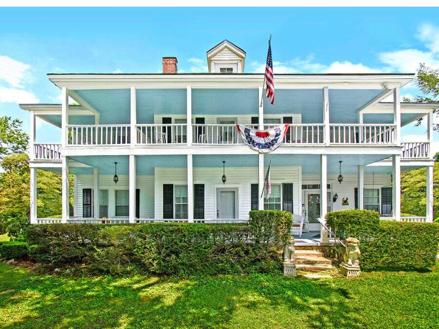 A two-story house with a porch, a flag, and a statue.