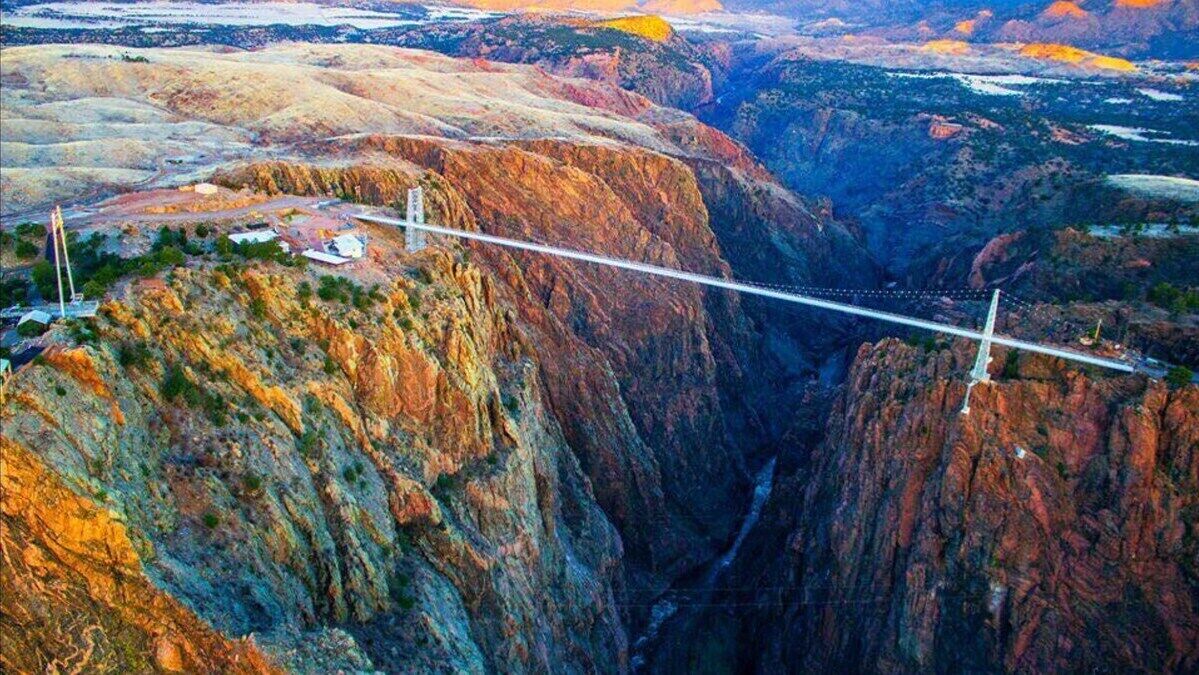 Un puente colgante sobre un cañón con terreno rocoso y vegetación escasa.