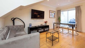 A living room with a sofa, a TV mounted on the wall, a glass coffee table, and a dining area with a table and chairs. - Brilliantly located 3BD Home Nr Paddington Station (London)