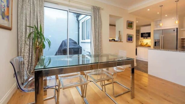 A modern kitchen with stainless steel appliances, a glass dining table with chairs, and a large window with curtains. - Brilliantly located 3BD Home Nr Paddington Station (London)