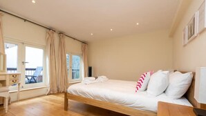 A bedroom with a wooden bed, a desk, and a chair, a window with curtains, and a view of the outdoors. - Brilliantly located 3BD Home Nr Paddington Station (London)