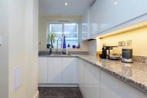 A modern kitchen with white cabinets, a granite countertop, and a window above the sink.