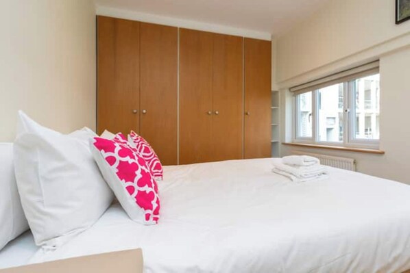 A bedroom with a bed, pillows, a window, and a wardrobe.