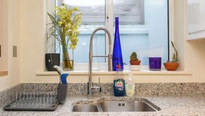 A kitchen with a double sink, a window with blinds, a vase with flowers, and a bottle of dish soap. - Brilliantly located 3BD Home Nr Paddington Station (London)