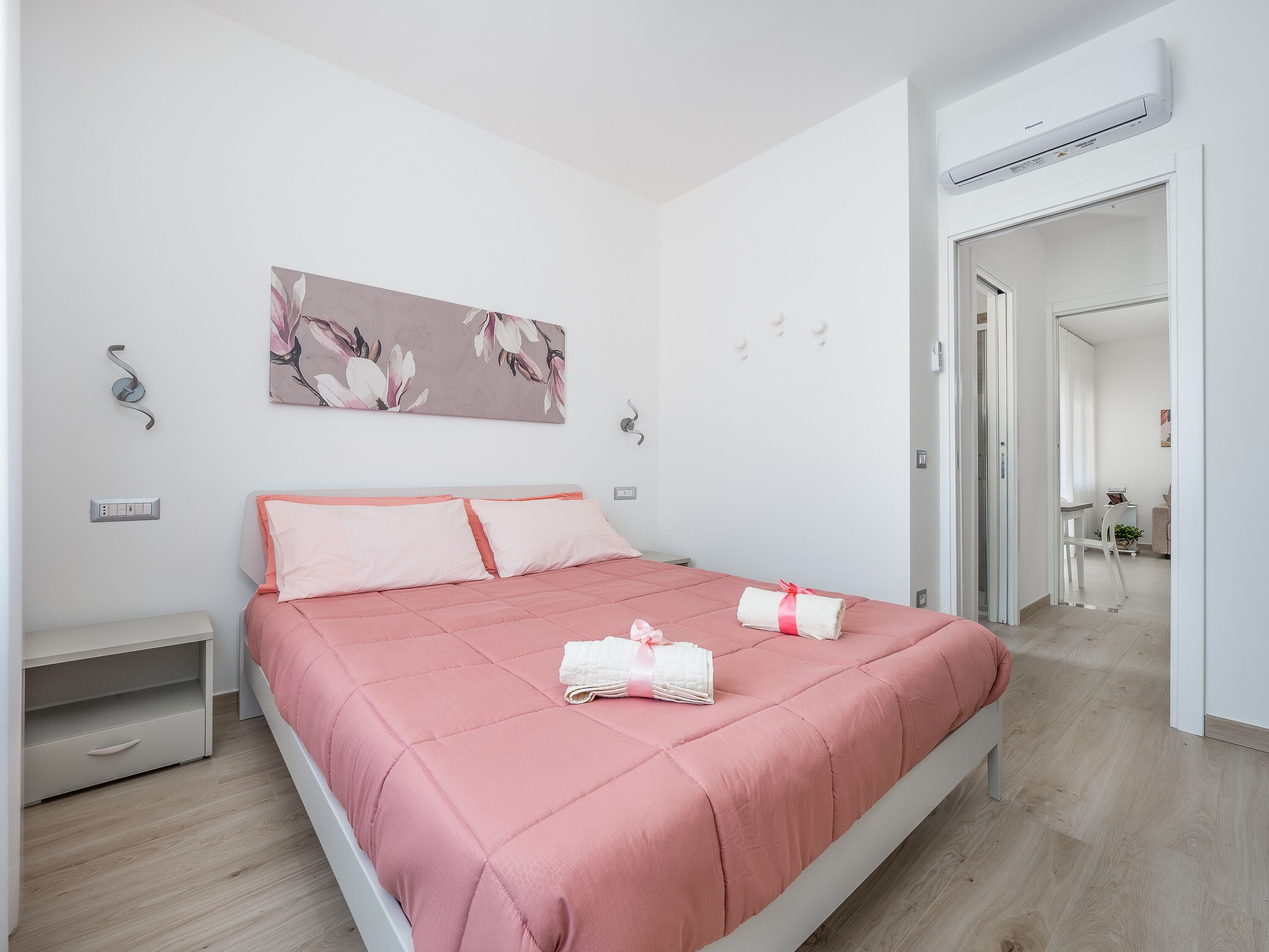 Une chambre moderne avec une couvre-lit rose, un climatiseur fixé au mur et une porte donnant sur la salle de bain.