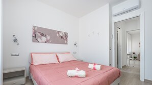 A modern bedroom with a pink bedspread, a wall-mounted air conditioner, and a door leading to a bathroom. - Harmony House (Piano di Sorrento)