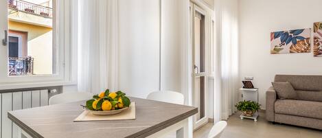 Un salon moderne avec un coin repas. On y voit une table avec un saladier rempli de citrons et une plante en pot. Un canapé et une petite table d’appoint avec une lampe sont également visibles.