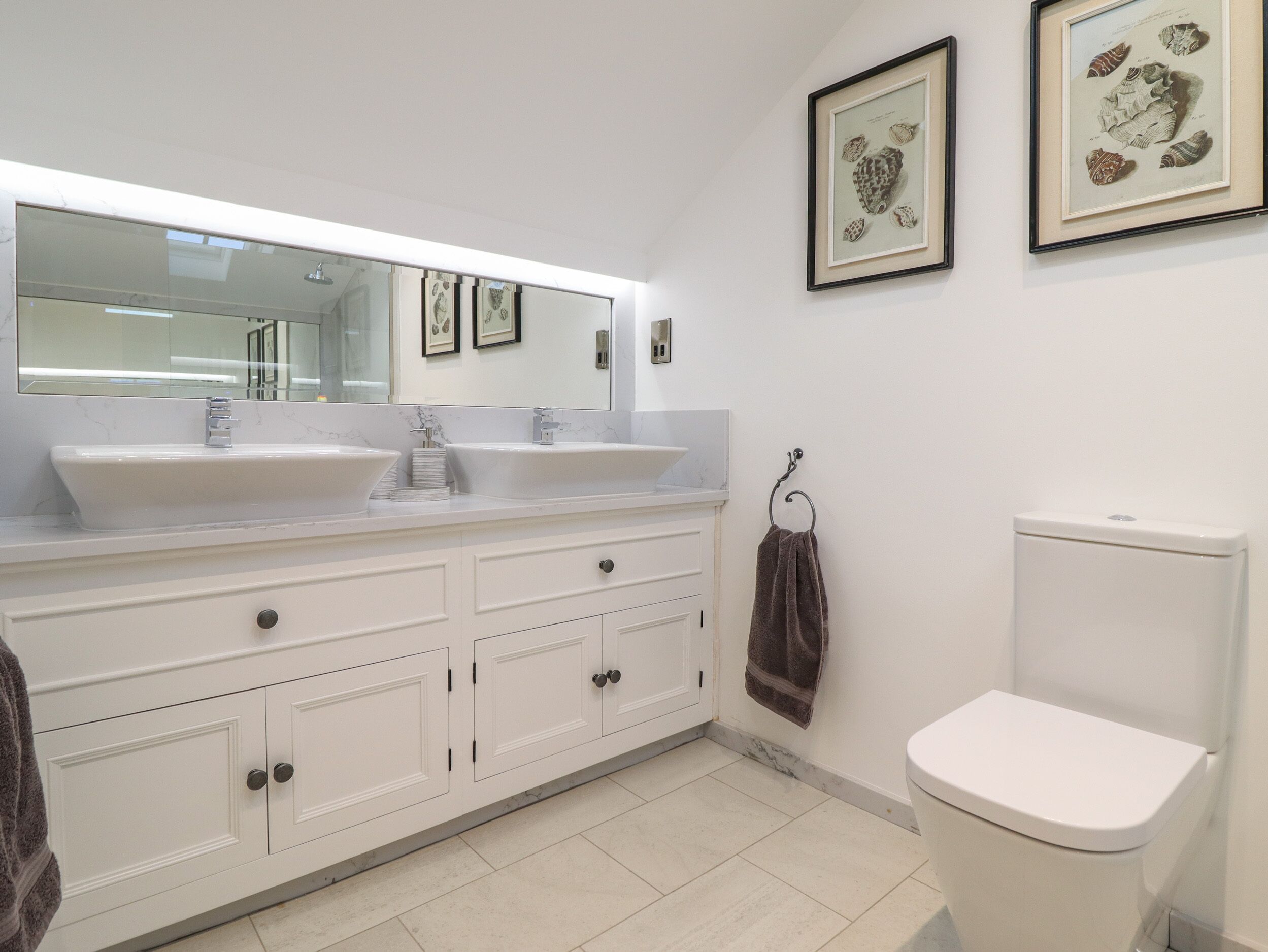 A modern bathroom with two sinks, a large mirror, and a toilet.
