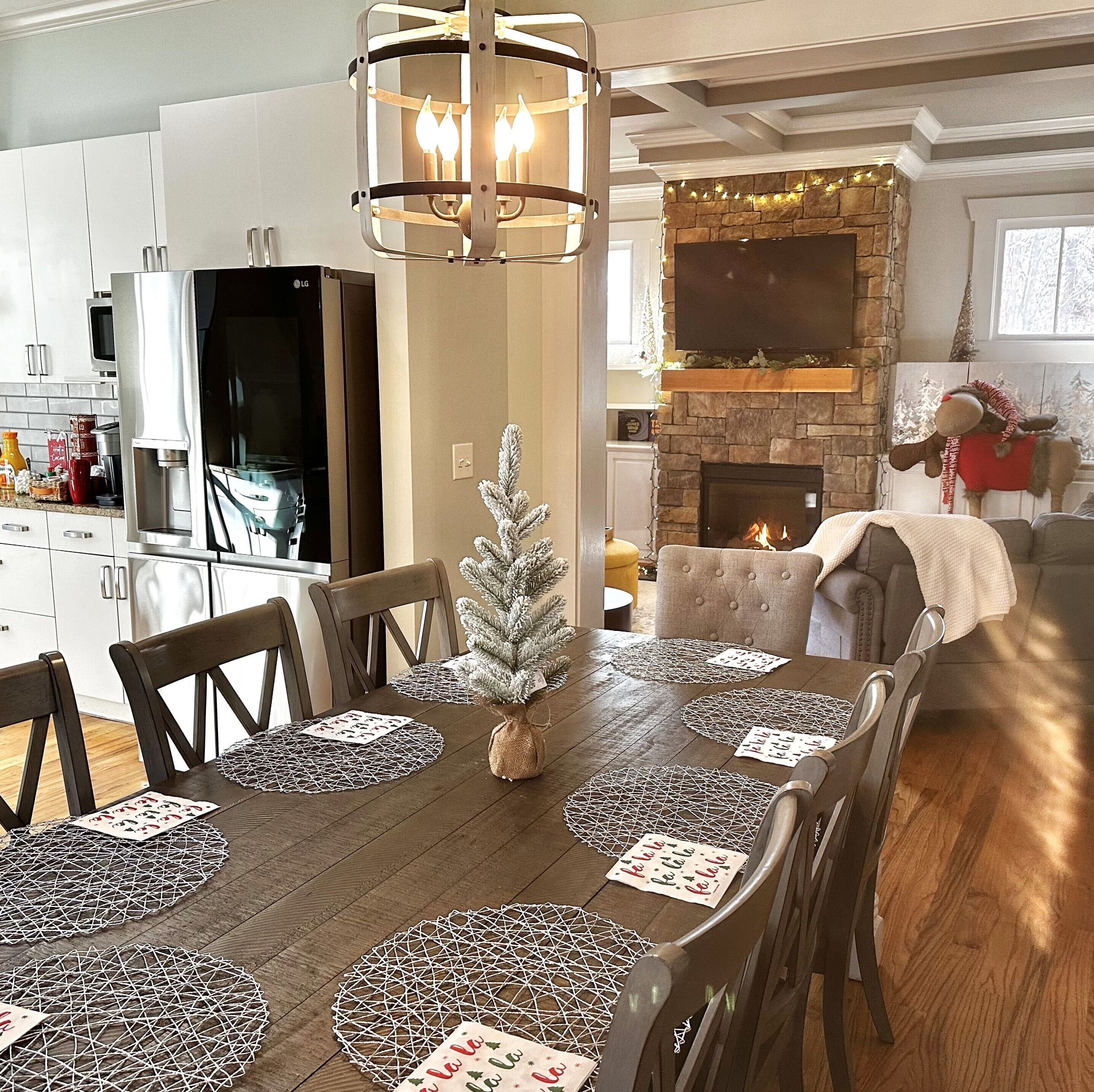 A dining area with a wooden table, chairs, and a small Christmas tree centerpiece.
