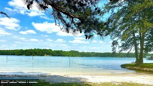 A lakeside view with a picnic table and a bench, surrounded by trees and a clear sky. - Buford Forest Retreat- Fire Pit - 5 bdrms- Sleeps 13 - Water Park, Venues, Golf! (Buford)