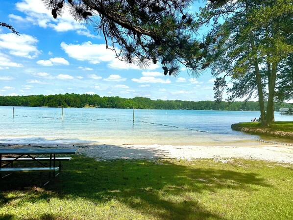A lakeside view with a picnic table and a bench, surrounded by trees and a clear sky.