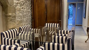 A dining area with striped chairs and a glass table, a stone wall, wooden doors, and a hallway leading to an outdoor area. - LA RENAUDIERE, HYPER CENTER (L'Isle-sur-la-Sorgue)