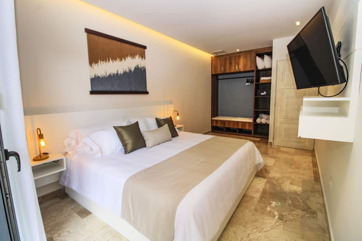 A modern hotel room with a large bed, a mounted TV, a wardrobe, and a painting on the wall.