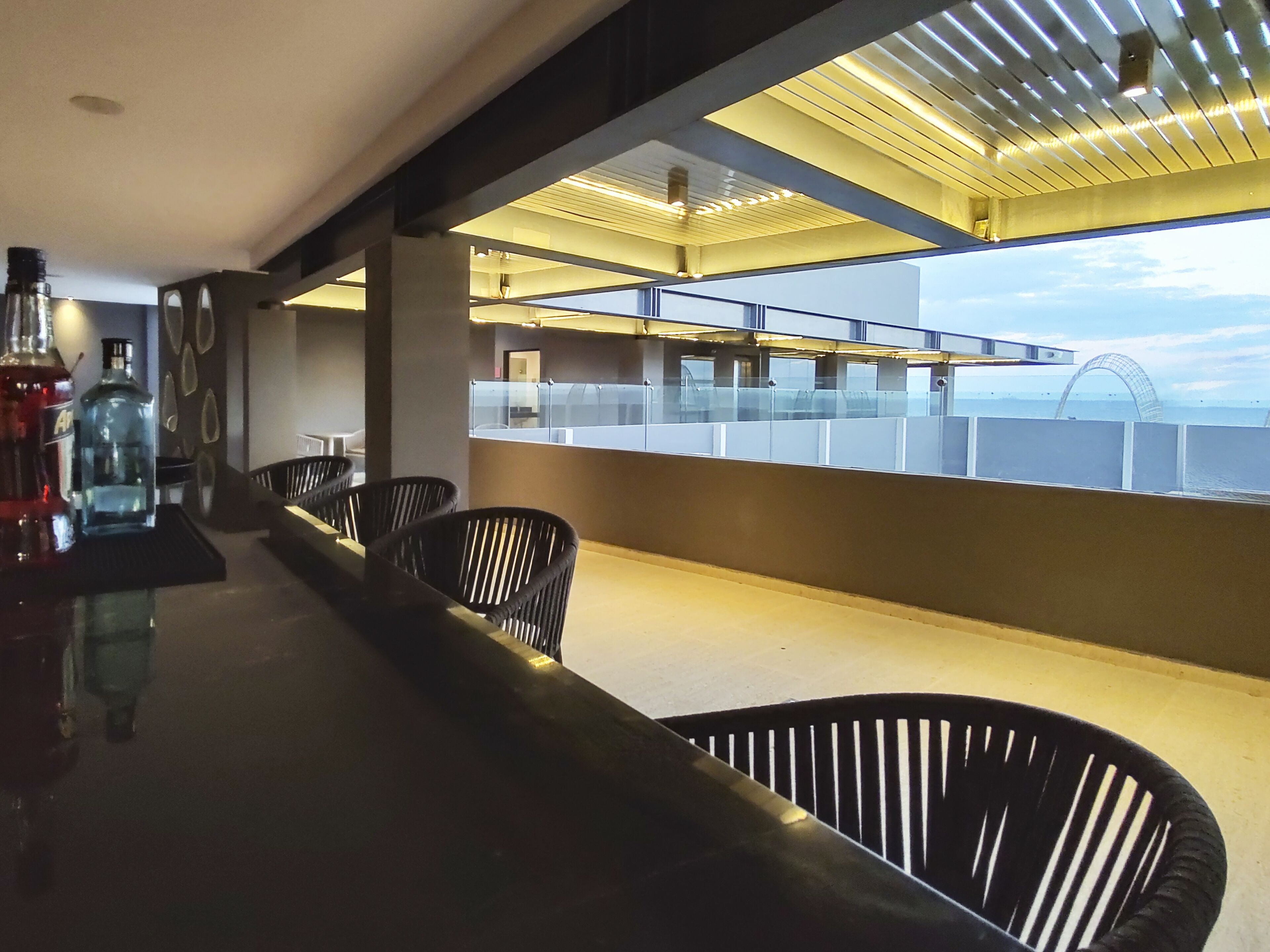 Eine Bar mit einer langen Theke, schwarzen Stühlen und Meerblick durch eine Glasscheibe.