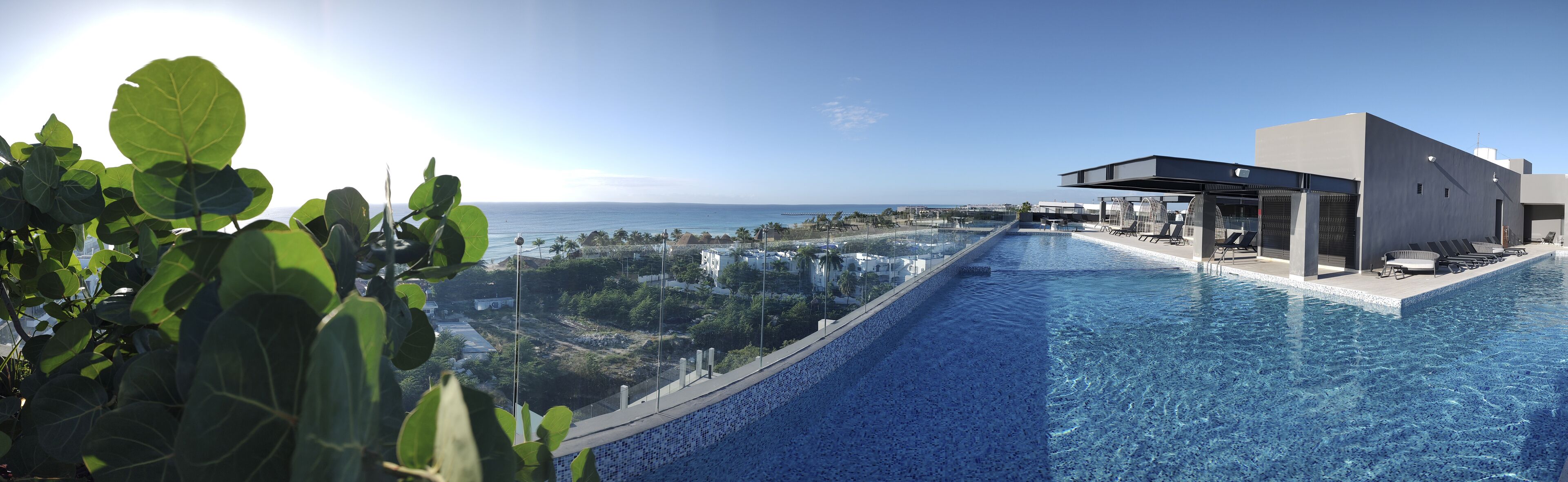Una piscina infinita moderna con vistas despejadas al océano y un edificio con asientos al aire libre.