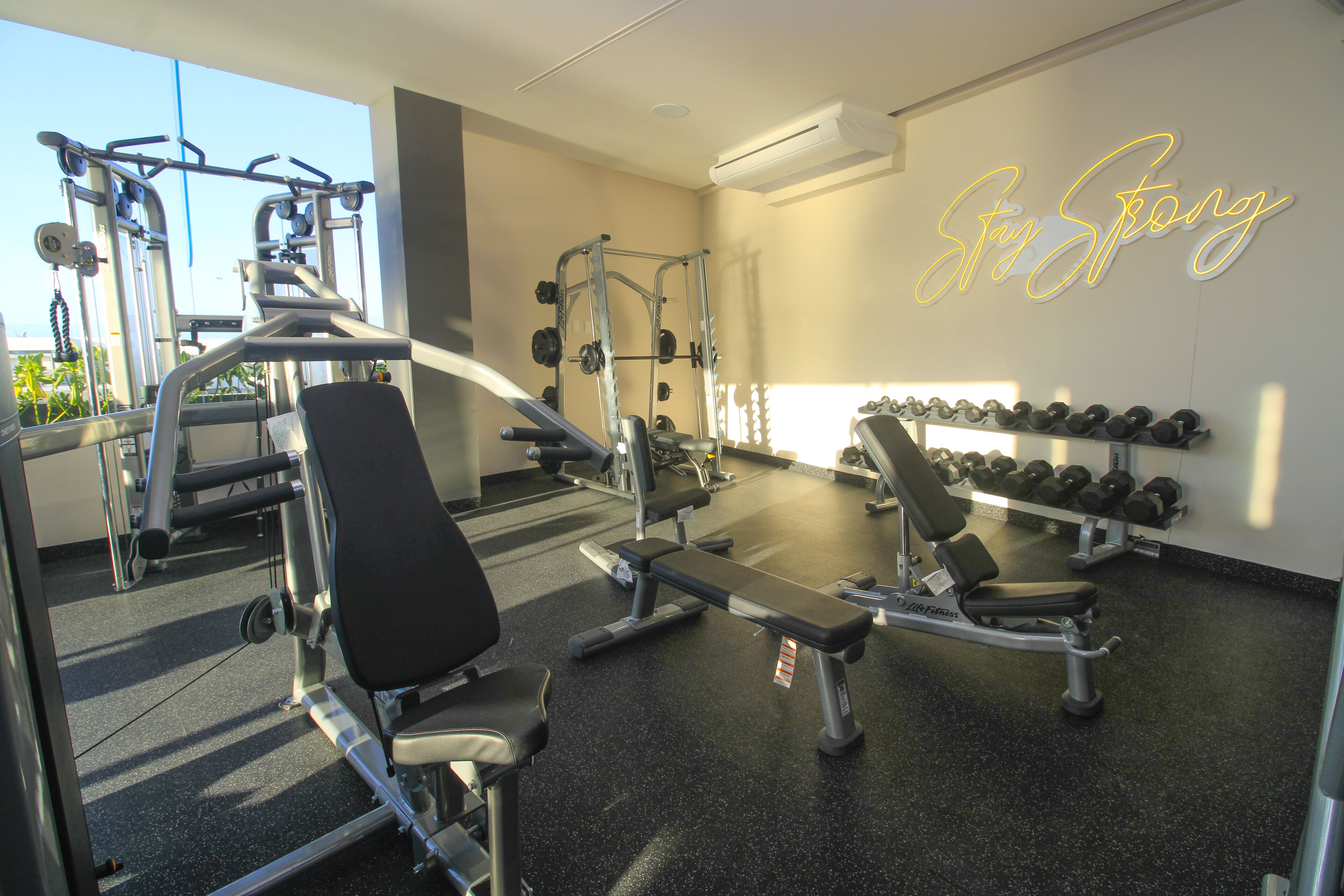 Ett gym med olika typer av träningsredskap, en bänk och en vägg med ett motiverande citat.