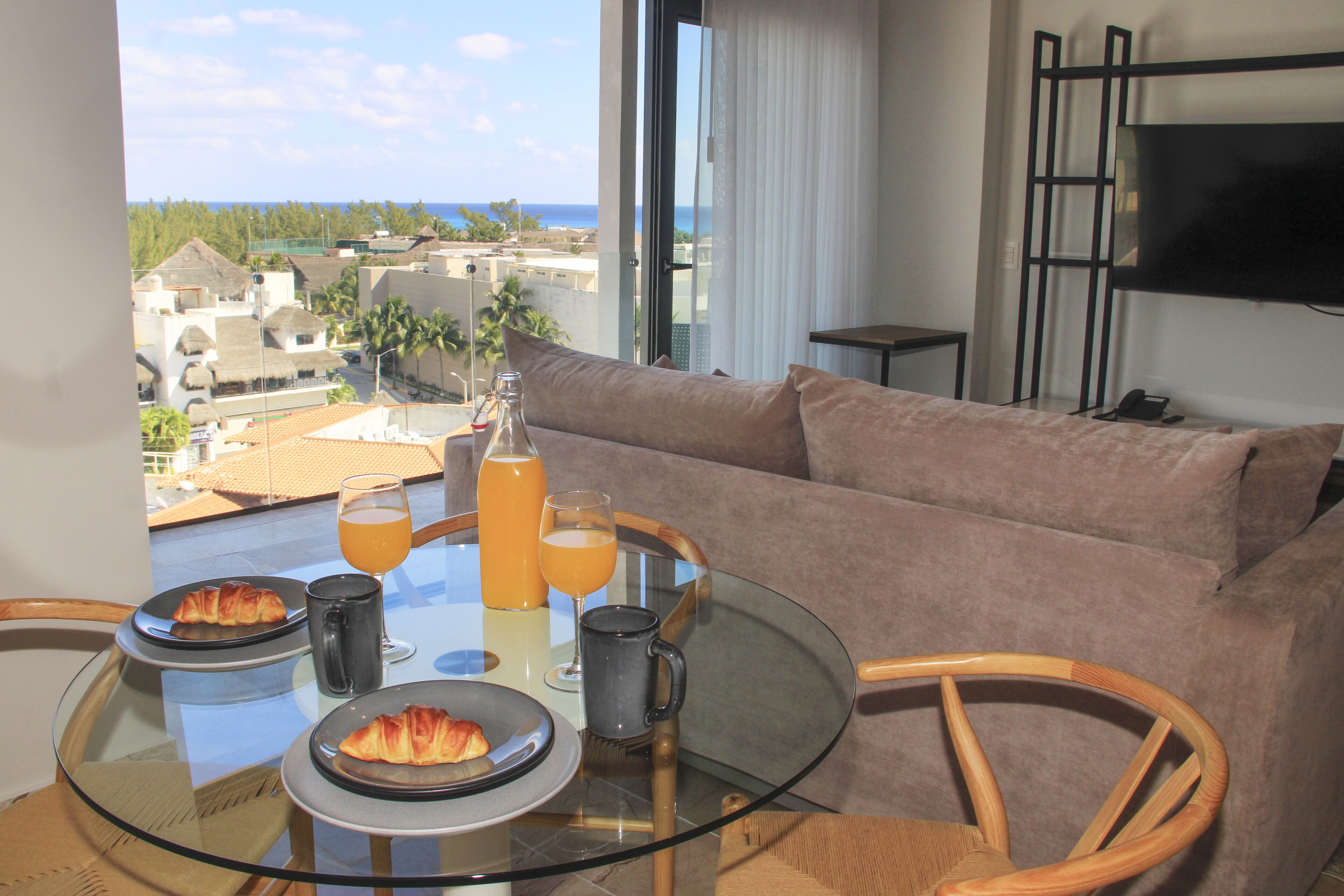 En balkon med et glastabel dækket til morgenmad, inklusive croissanter, juice og kaffe.