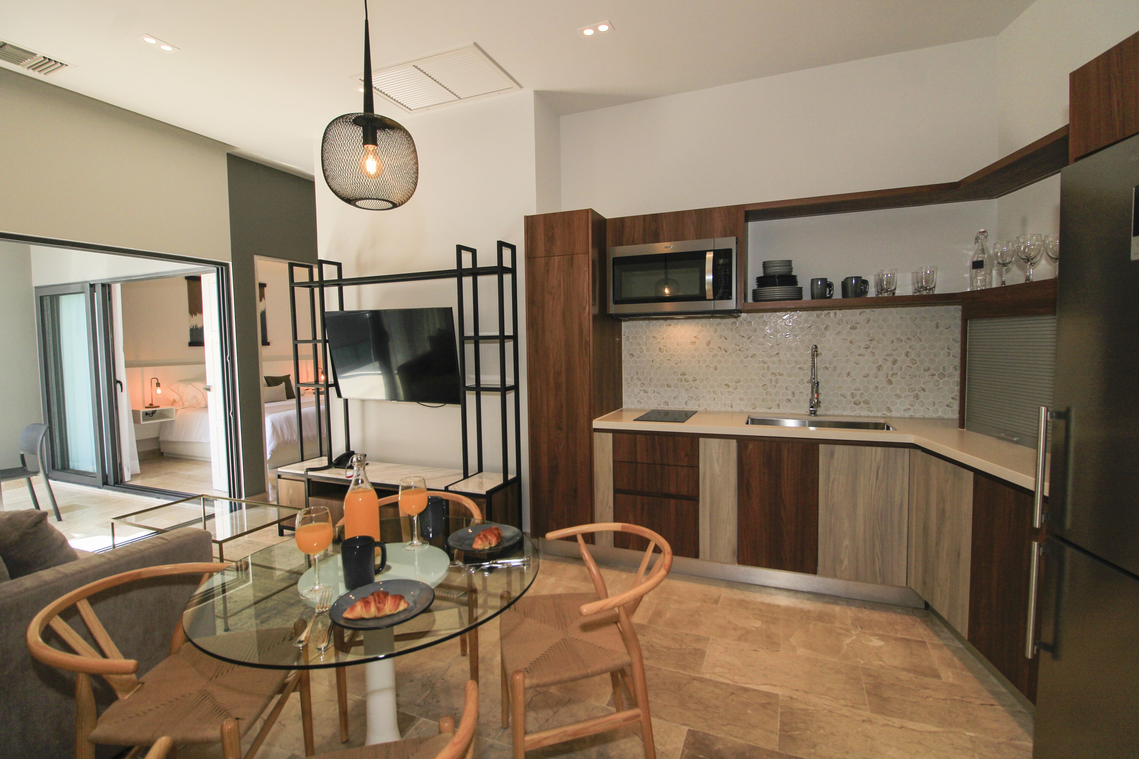 A modern kitchen with a glass dining table, wooden chairs, a TV, and a microwave.