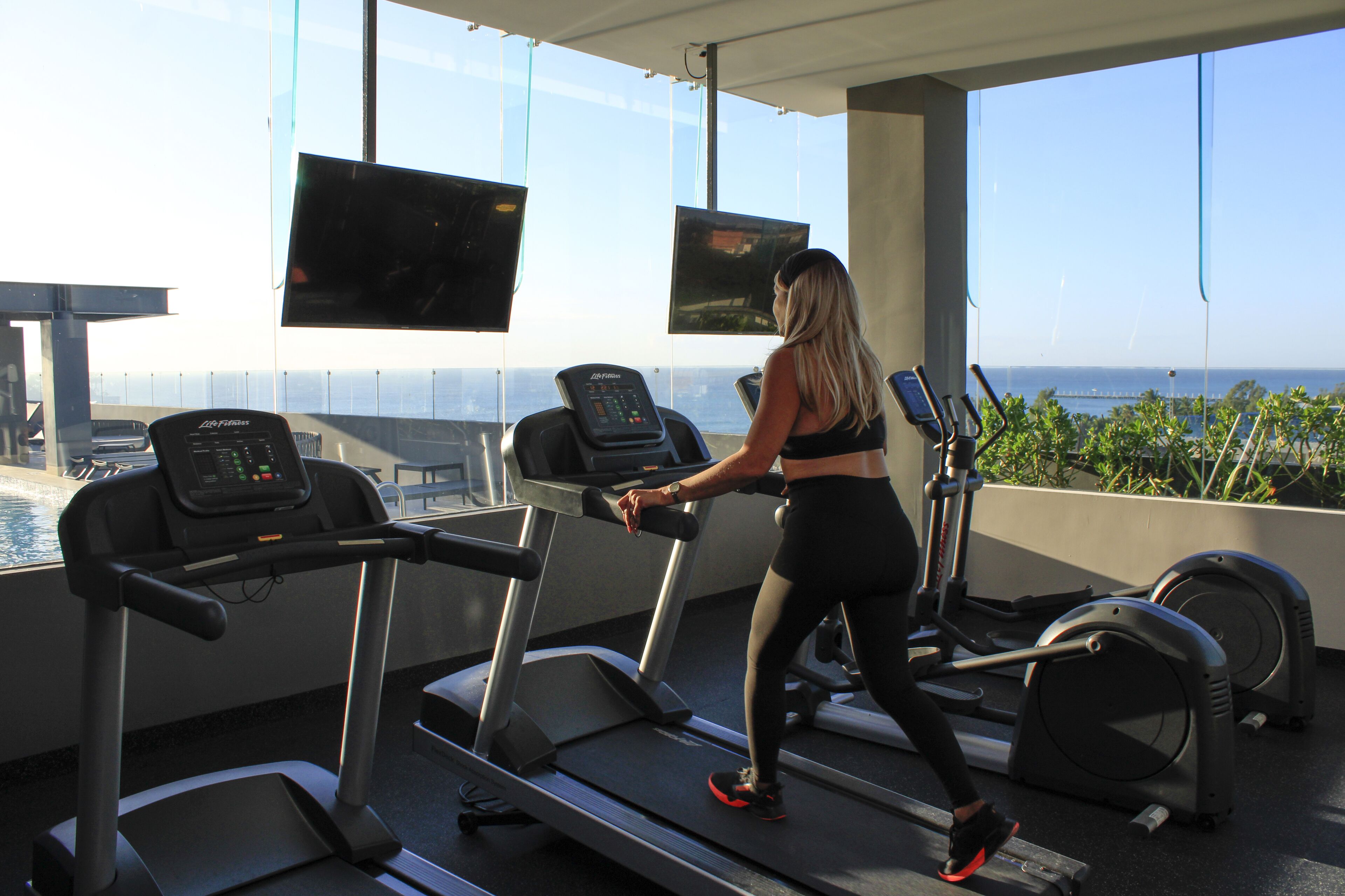 A gym with treadmills and exercise equipment, large windows, and a view of the ocean.