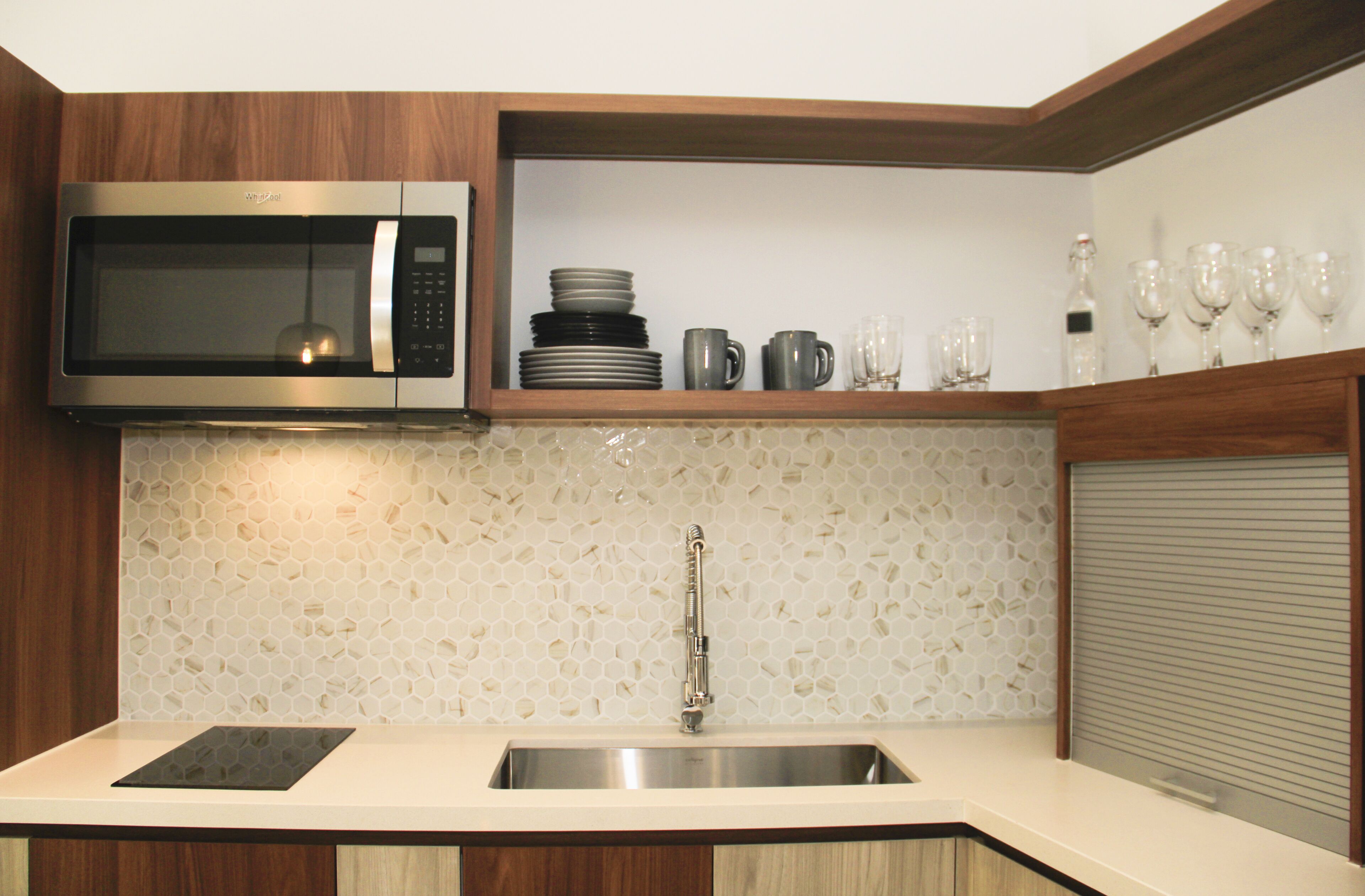 A kitchen with a microwave, sink, and a shelf with plates and glasses.