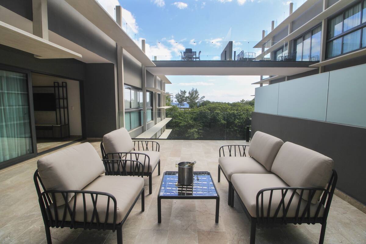 A modern outdoor seating area with a table and chairs, a view of the sky, and a balcony with a railing.