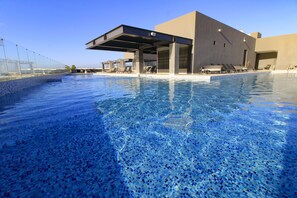 Ein moderner Poolbereich mit klarem, blauem Wasser, Liegestühlen und einer überdachten Sitzgelegenheit.