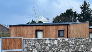 A building with a stone wall and wooden panels, a metal gate, and a windmill in the background. - Tiny House Glamping - On the Wild Atlantic Way 5 minutes from Tralee (Tralee)