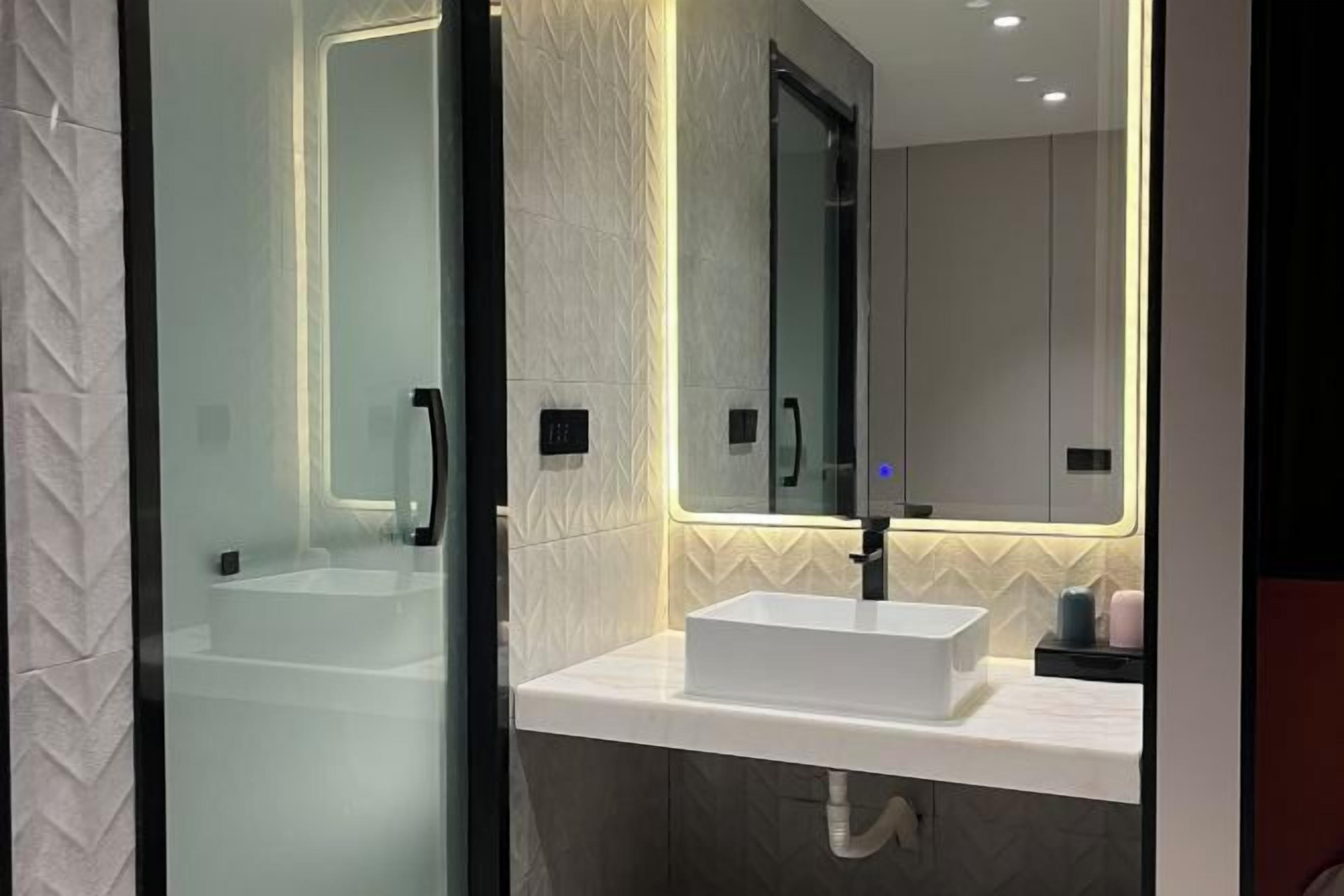 A modern bathroom with a glass shower enclosure, a white sink, and a mirror above it.