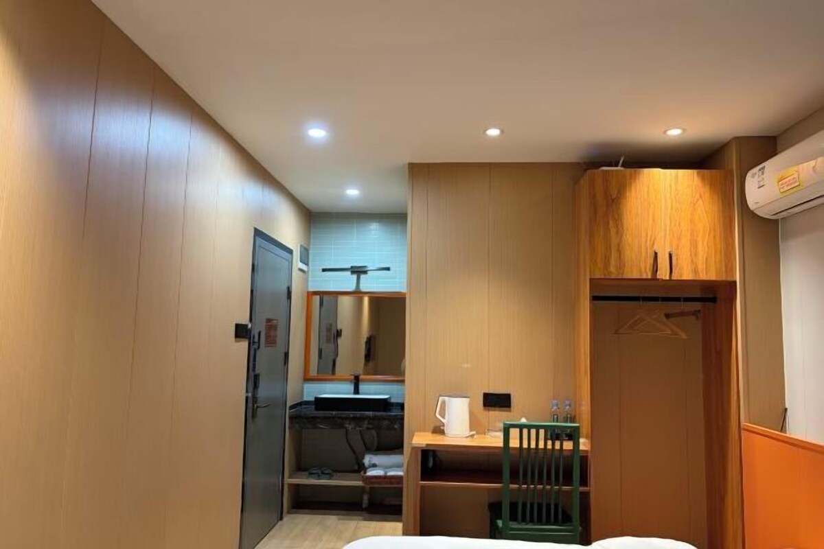 Habitación de hotel con cama, escritorio, silla, armario y baño con espejo y lavamanos.
