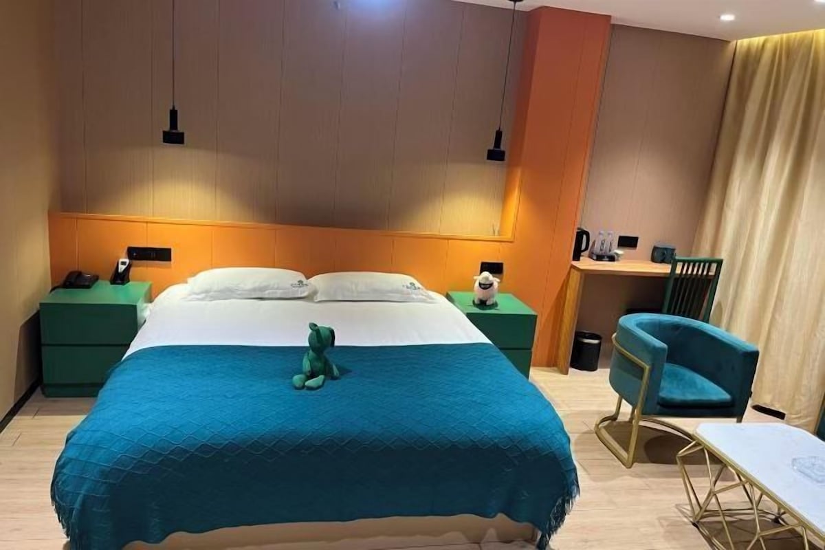 A hotel room with a bed, green nightstands, a desk, a chair, and a small table.