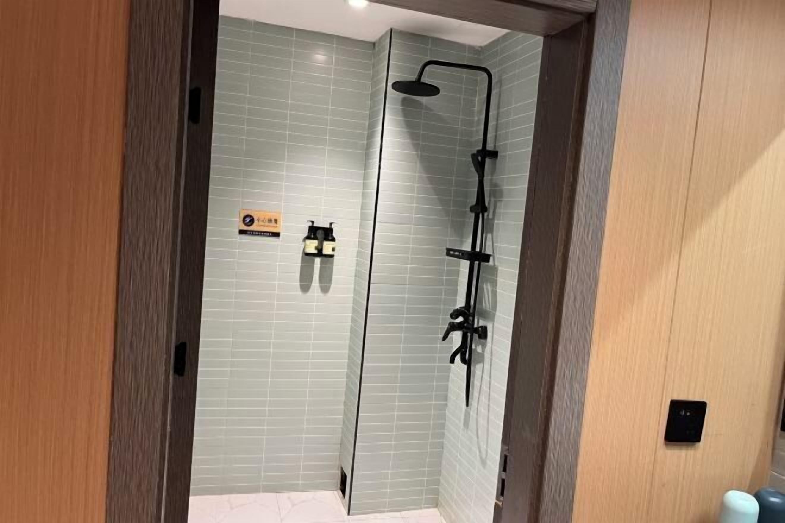 A modern bathroom with a glass shower enclosure, a towel rack, and a sign indicating a 24-hour service.