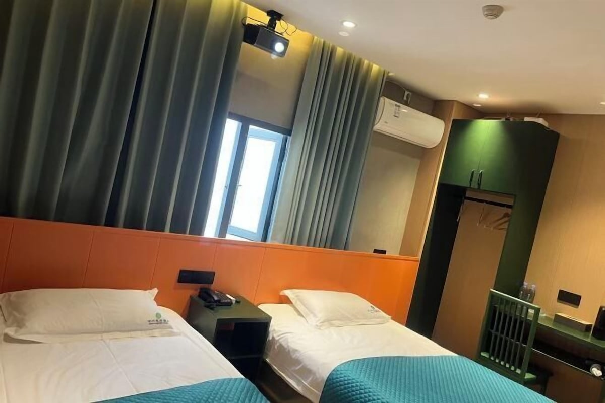 A hotel room with two beds, a desk, a chair, a mirror, and an air conditioning unit.