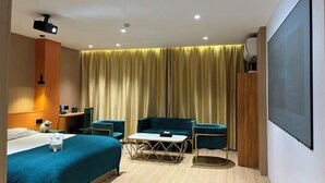A hotel room with a bed, a desk, a chair, a sofa, a coffee table, and a projector. - Ganmu Gardens Hotel (Susong)