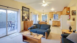 A cozy living room with a sofa, a coffee table, and a dining area with chairs. There is a kitchen in the background with wooden cabinets and a refrigerator. - Cave Bay Vacation Rental w/ Game Room! (Worley)