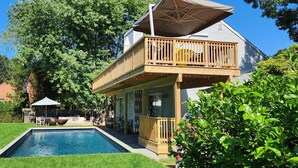 Une maison à deux étages dotée d’une terrasse en bois, d’une piscine et d’un patio aménagé avec du mobilier d’extérieur.