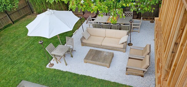 A patio area with a beige sofa, wooden chairs, a small table, and a large umbrella.