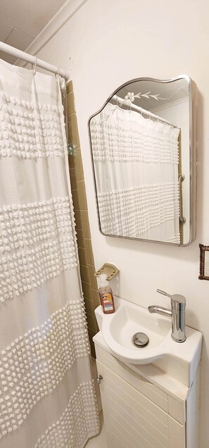 A bathroom with a shower curtain, a sink with a mirror, and a bottle of hand soap.