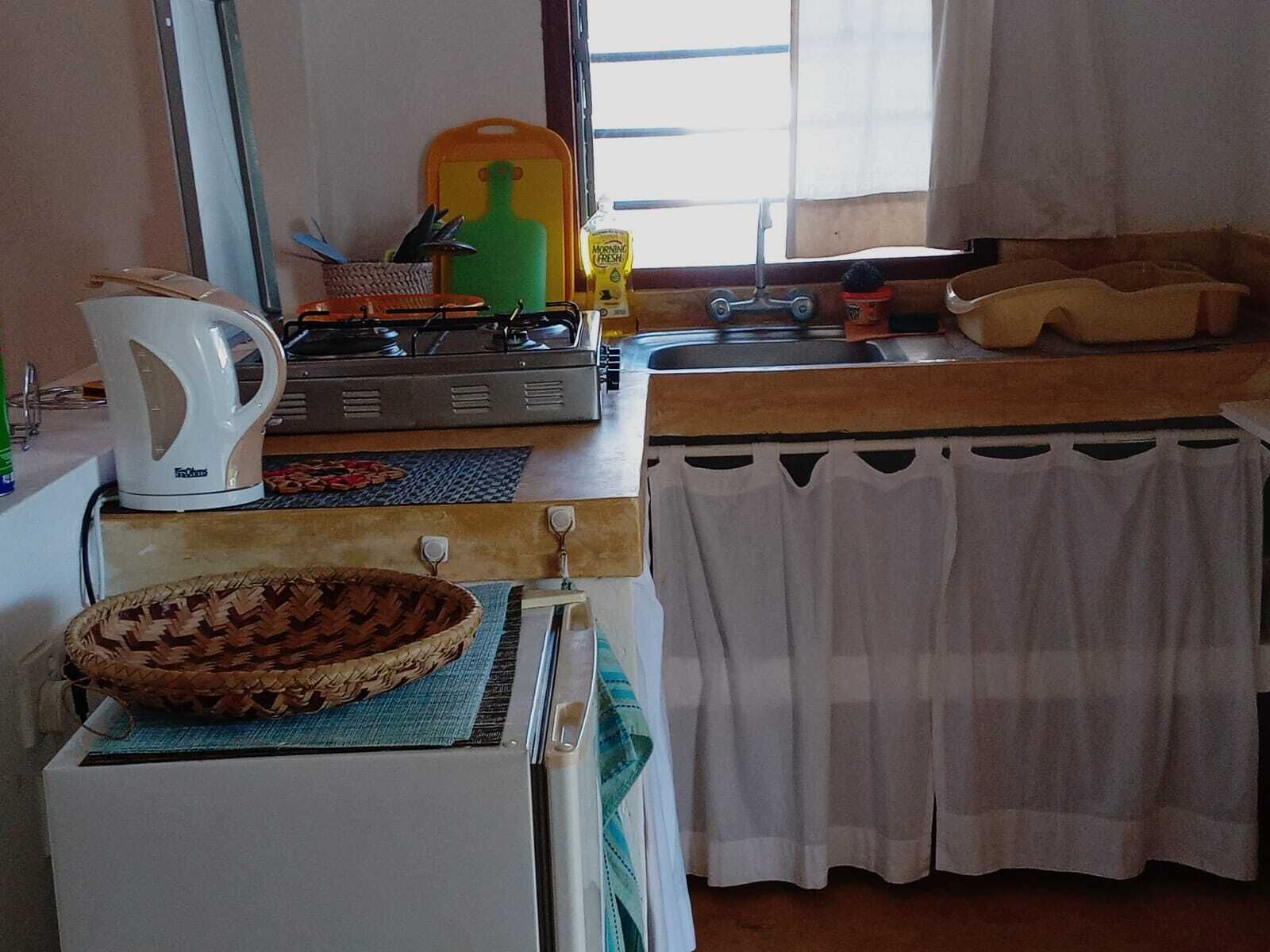 A compact kitchen with a stove, kettle, and a small sink.