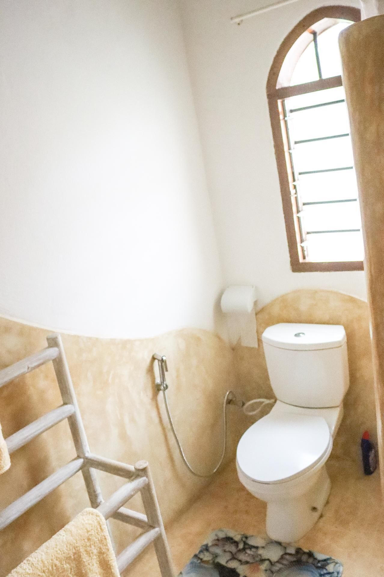 Et lille badeværelse med toilet, bruser og et vindue.