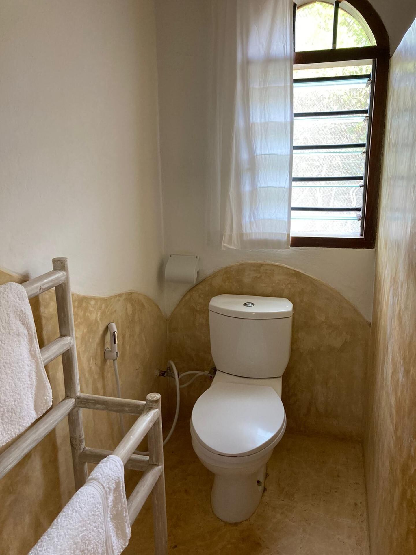 Une petite salle de bain compacte, comprenant des toilettes, un espace douche et une fenêtre avec des stores.
