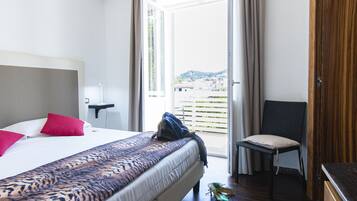 A hotel room with a bed, a chair, a desk, and a view of the city.