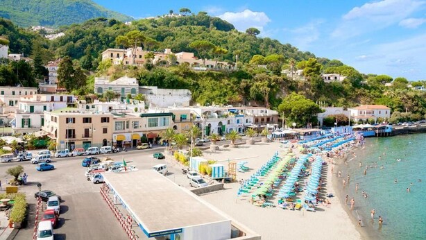 Uma cidade costeira com praia, carros estacionados e edifícios.