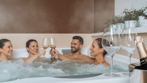 Um grupo de pessoas em uma banheira de hidromassagem com taças de champanhe e uma garrafa.