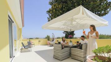 Una terraza con asientos al aire libre, un toldo grande y vista al mar.