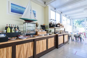 A breakfast bar with a wooden finish, a glass display case with food items, and a view of the outdoors through large windows. - Marina 10 boutique&design hotel (Casamicciola Terme)