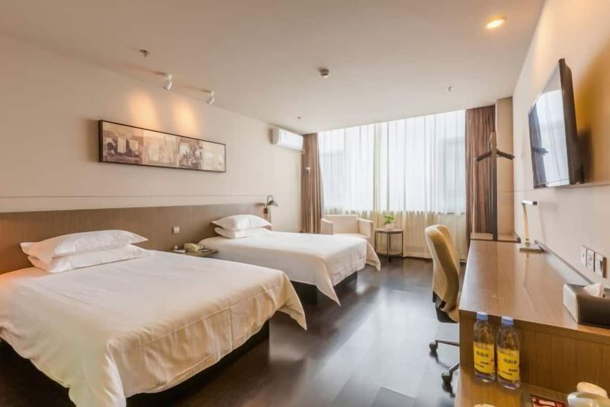 A hotel room with two beds, a desk, a chair, a TV, and a window with curtains.